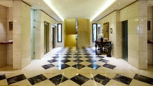 A hotel lobby with a checkered floor, elevators, a staircase, and a reception desk. - PROMENADE HOTEL ZALKA (Zalqa)