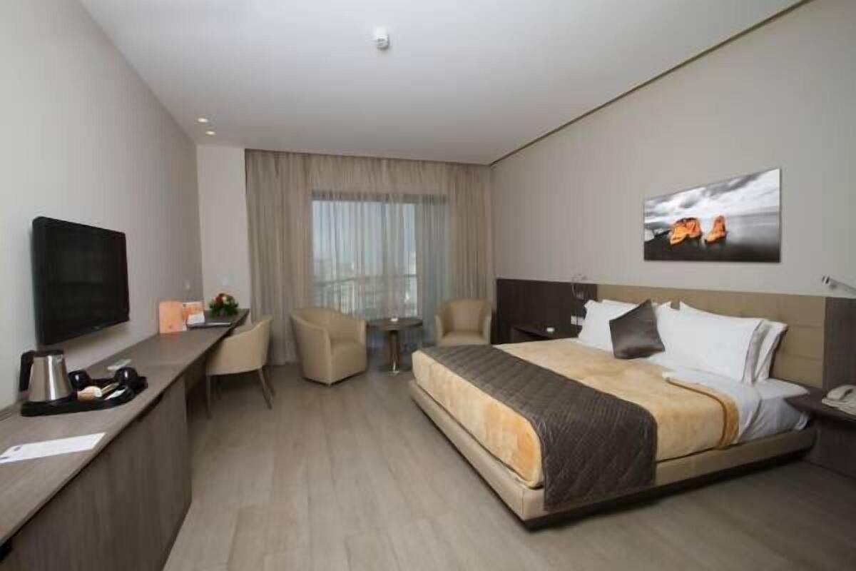 Una habitación de hotel con cama, escritorio con cafetera, televisor y un cuadro en la pared.