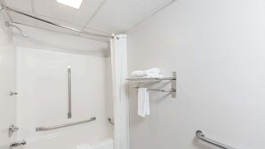 Un baño con ducha, barras de apoyo, toallero y retrete.