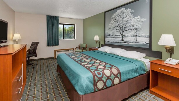 Habitación de hotel con cama, escritorio, silla y un ventanal grande.