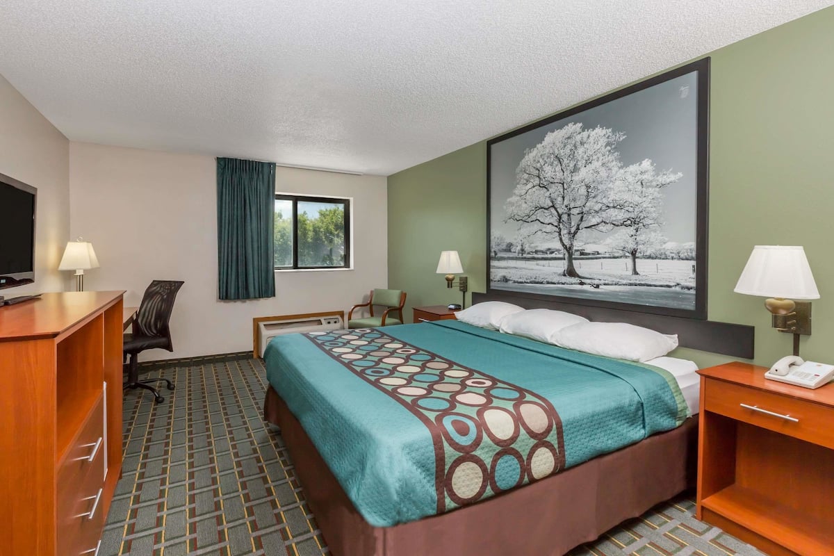 A hotel room with a bed, desk, chair, and a large window.