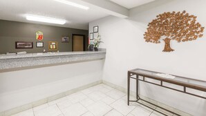 Un área de recepción con mostrador, certificados enmarcados, decoración de árbol montada en la pared y una escalera con barandilla de vidrio.