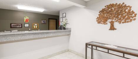A reception area with a counter, framed certificates, a wall-mounted tree decoration, and a staircase with a glass railing.