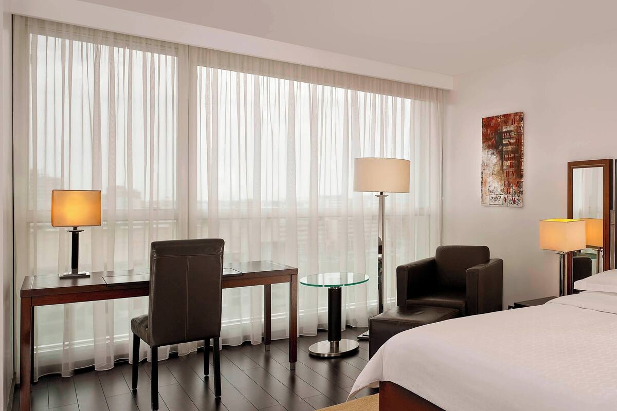 Ein Hotelzimmer mit einem Bett, zwei Sesseln, einem kleinen Tisch, einem Glastisch und zwei Lampen.