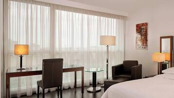 Habitación de hotel con cama, dos sillas, una mesita, una mesa de centro de vidrio y dos lámparas.