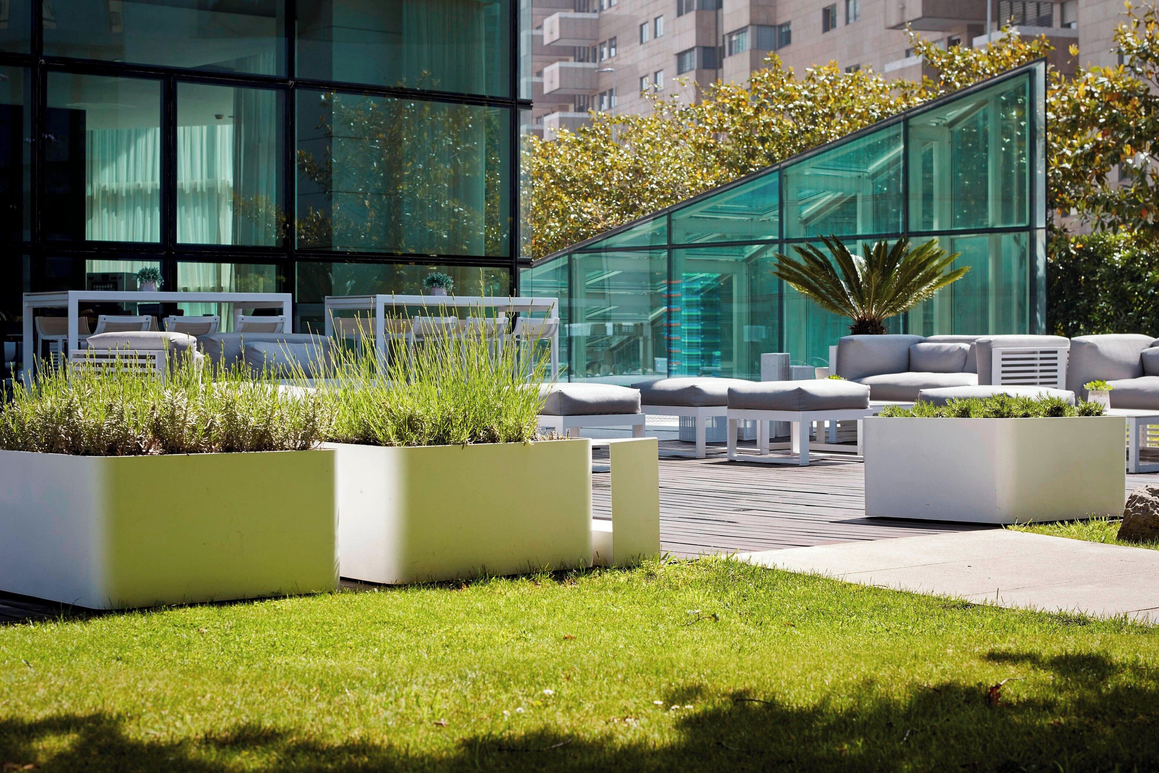 Un área de estar exterior moderna con mobiliario blanco y jardineras con plantas.