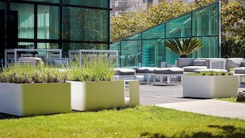 Un área de estar exterior moderna con mobiliario blanco y jardineras con plantas.