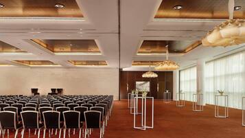 Un salón de conferencias con hileras de sillas, un escenario y un diseño de techo moderno.
