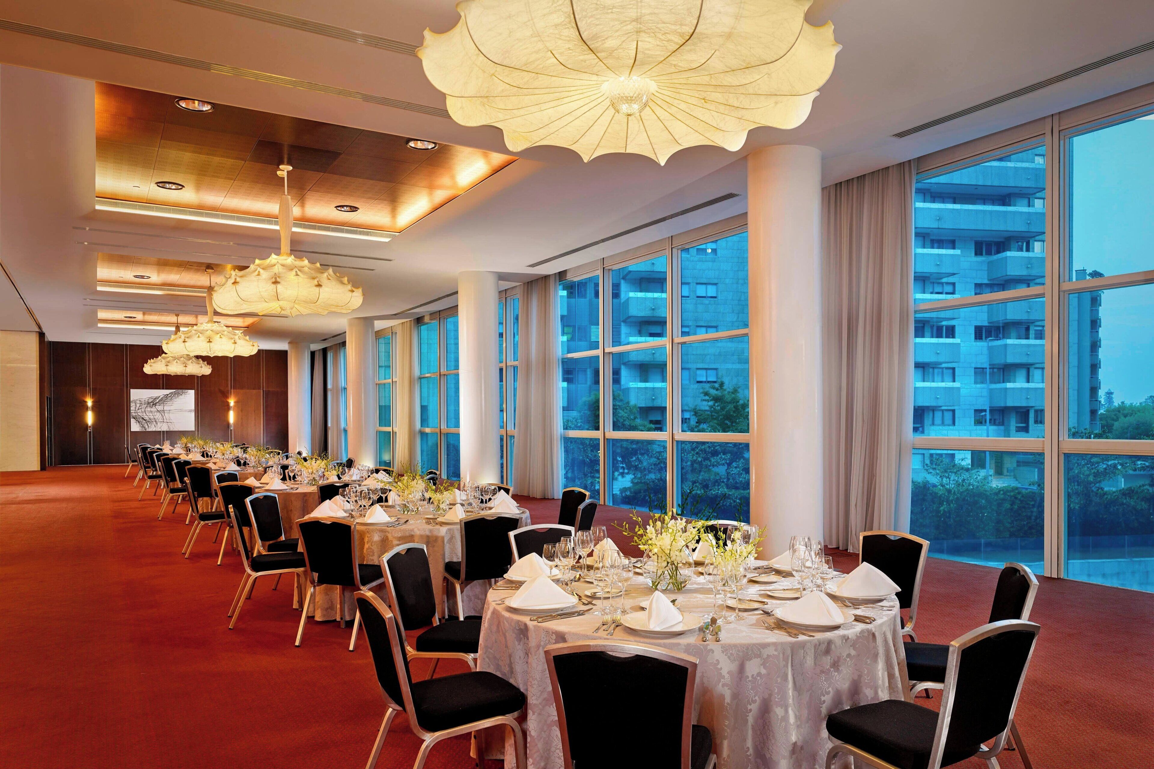 Une salle de banquet avec des tables rondes dressées pour le repas, de grandes fenêtres et des lustres modernes.