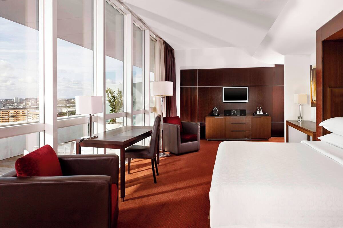 Ein Hotelzimmer mit einem großen Bett, einem Schreibtisch mit Stuhl, einem Fernseher und einer Minibar.