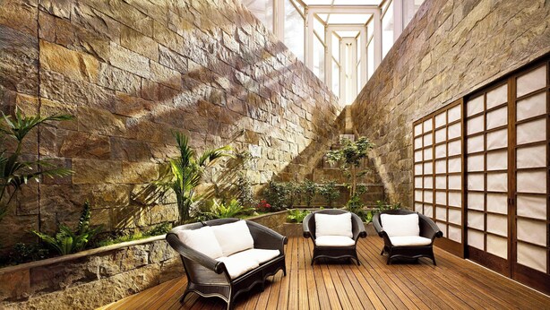 Un espacio interior con paredes de piedra, suelo de madera y dos sillas de mimbre con cojines blancos.