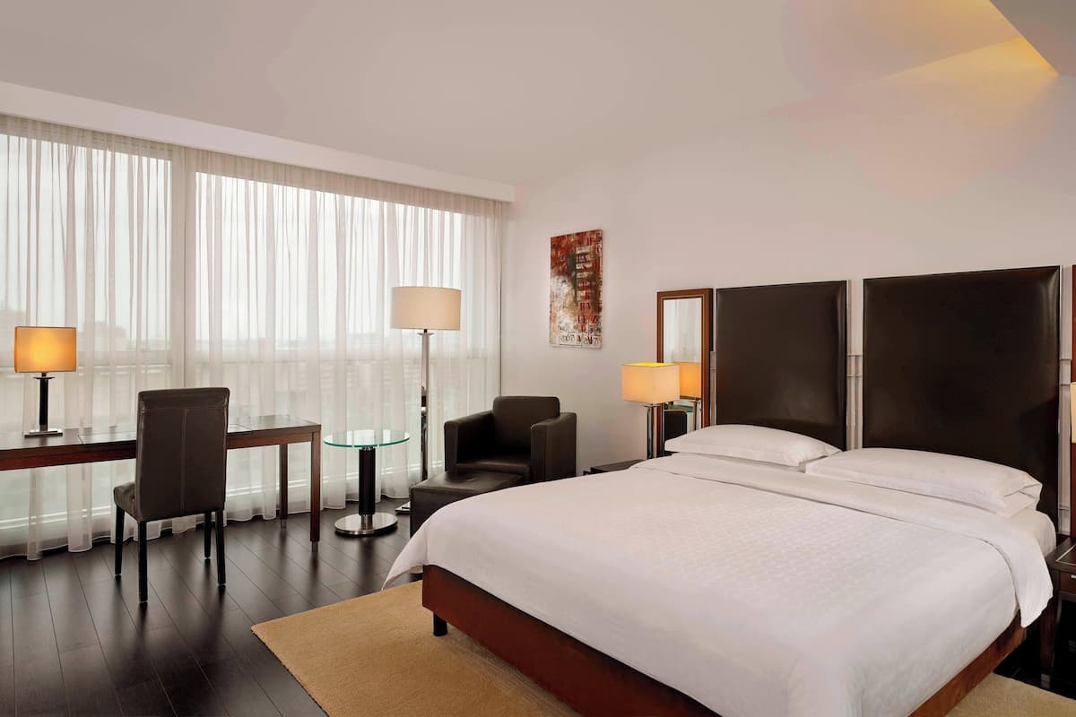Ein Hotelzimmer mit einem großen Bett, einem Schreibtisch mit Stuhl, einem kleinen Tisch und einer Lampe.