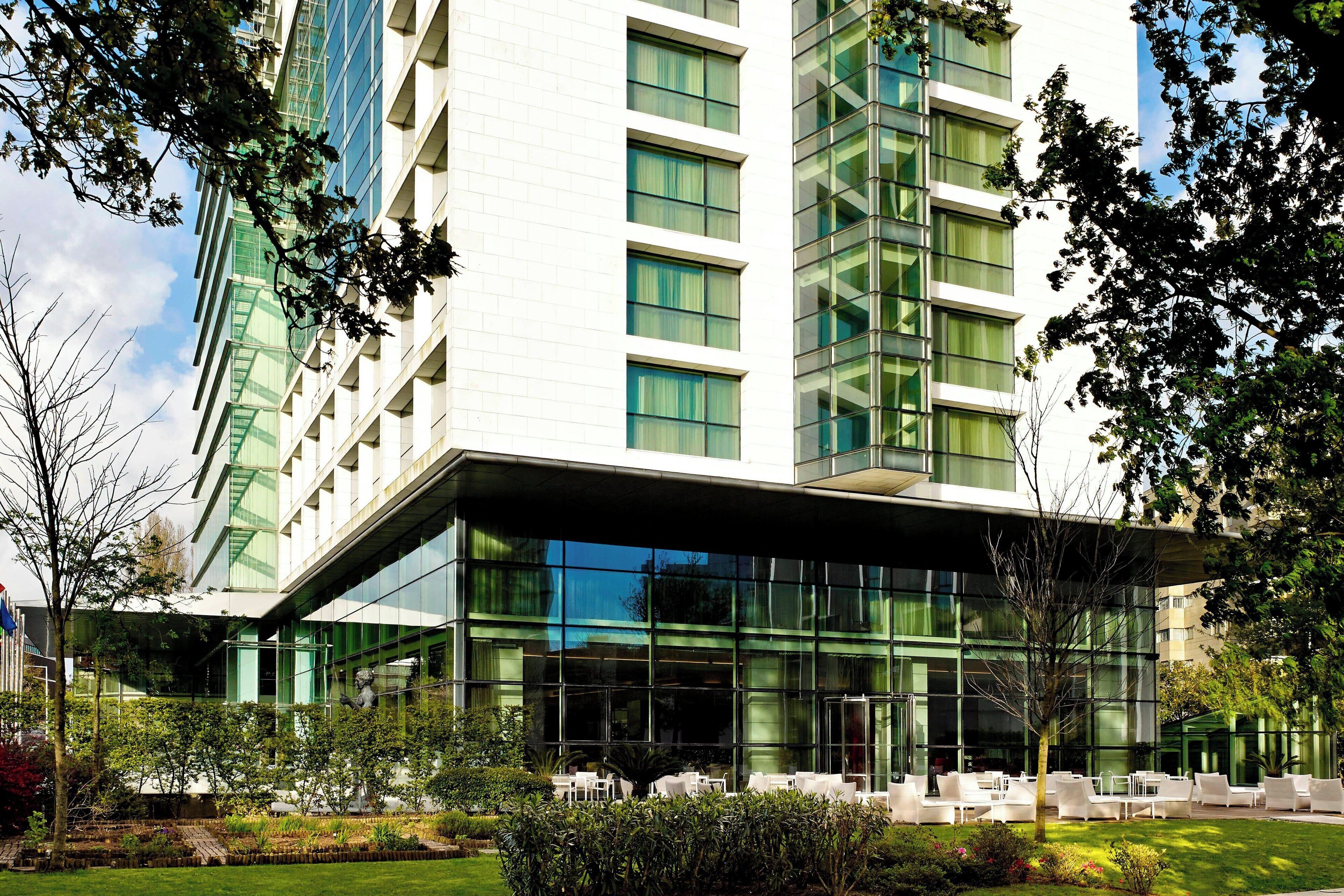 Un hotel moderno con fachada de vidrio, zona de estar al aire libre y jardines bien cuidados.