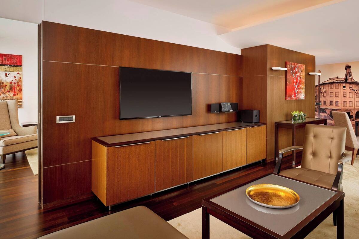 Ein modernes Wohnzimmer mit Flachbildfernseher an einer Holzwand, einer integrierten Unterhaltungsecke und einem Essbereich mit Tisch und Stühlen.