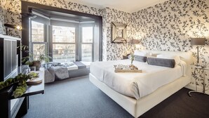 A modern bedroom with a large bed, a small seating area, and a view of the outside.