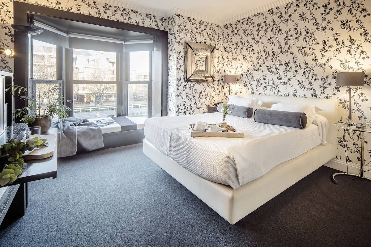 A modern bedroom with a large bed, a small seating area, and a view of the outside.
