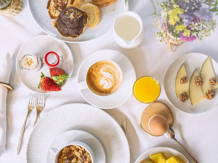 Desayuno con diversas comidas y bebidas sobre una mesa blanca.
