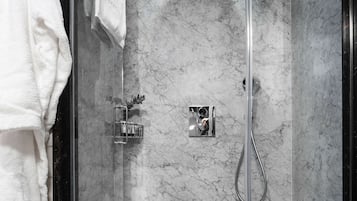 Una ducha moderna con puerta de vidrio, paredes de mármol y una bañera blanca.
