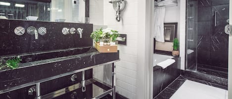 A modern bathroom with a black marble sink, a hairdryer mounted on the wall, and a glass-enclosed shower area.