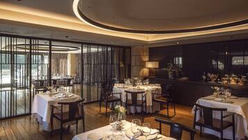 A modern dining area with round tables, white tablecloths, and a view through a patterned glass partition.