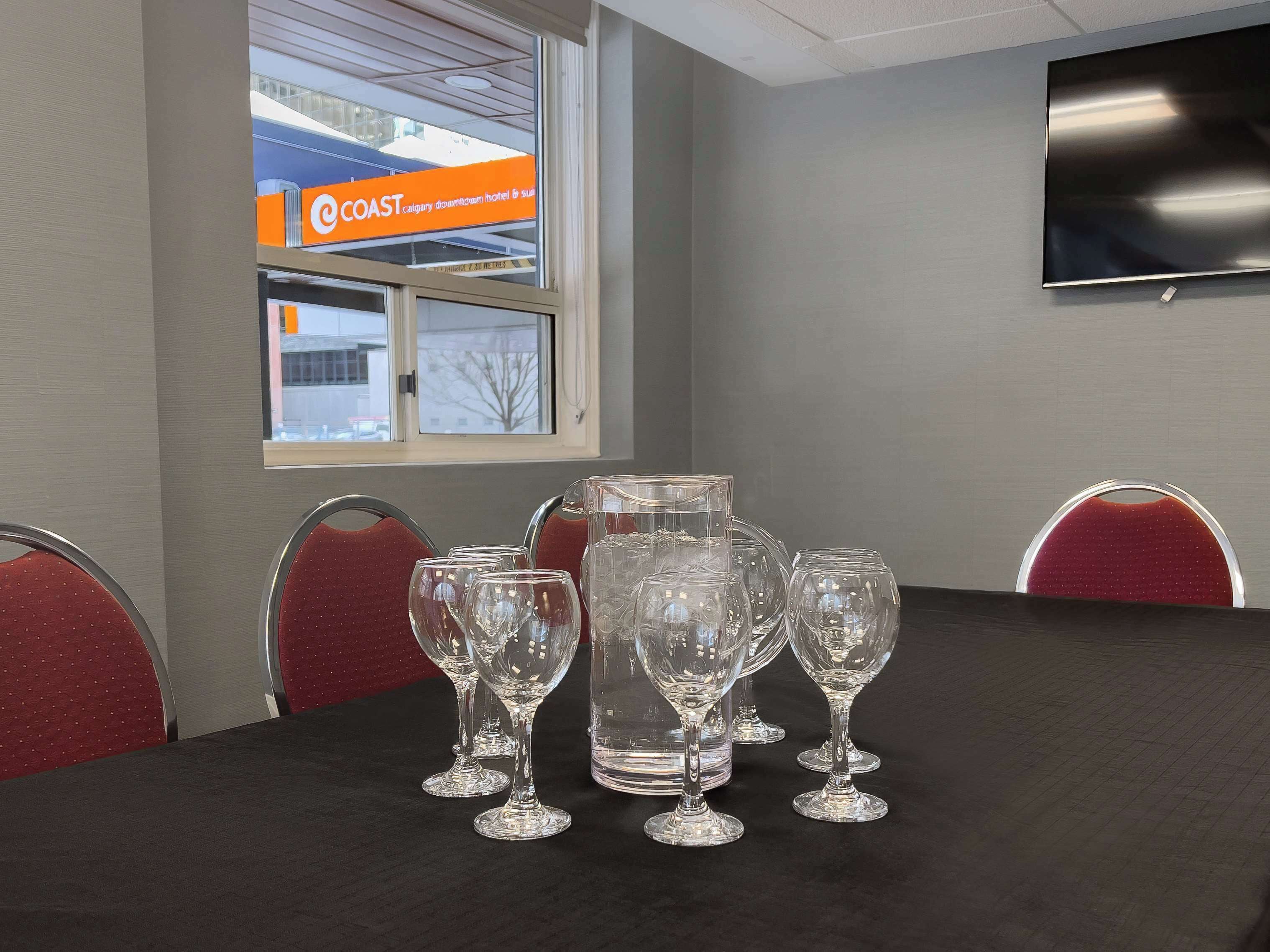 A conference room with a table set for a meeting, featuring a large crystal decanter, multiple wine glasses, and red upholstered chairs.