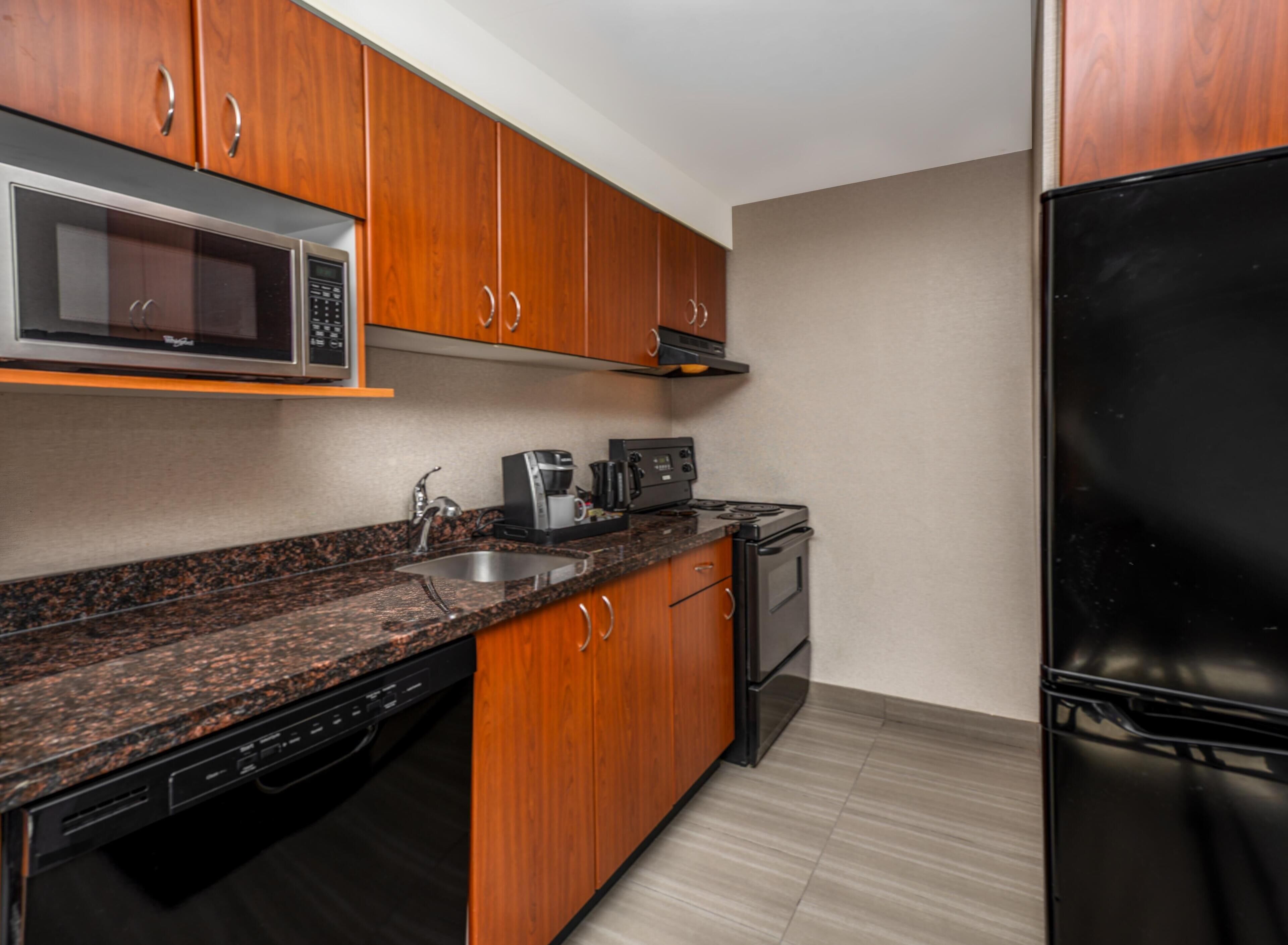 A modern kitchen with wooden cabinets, a stainless steel microwave, a coffee maker, a stove, and a black refrigerator.