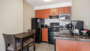 A compact kitchen with wooden cabinets, a refrigerator, a microwave, an oven, and a coffee maker.