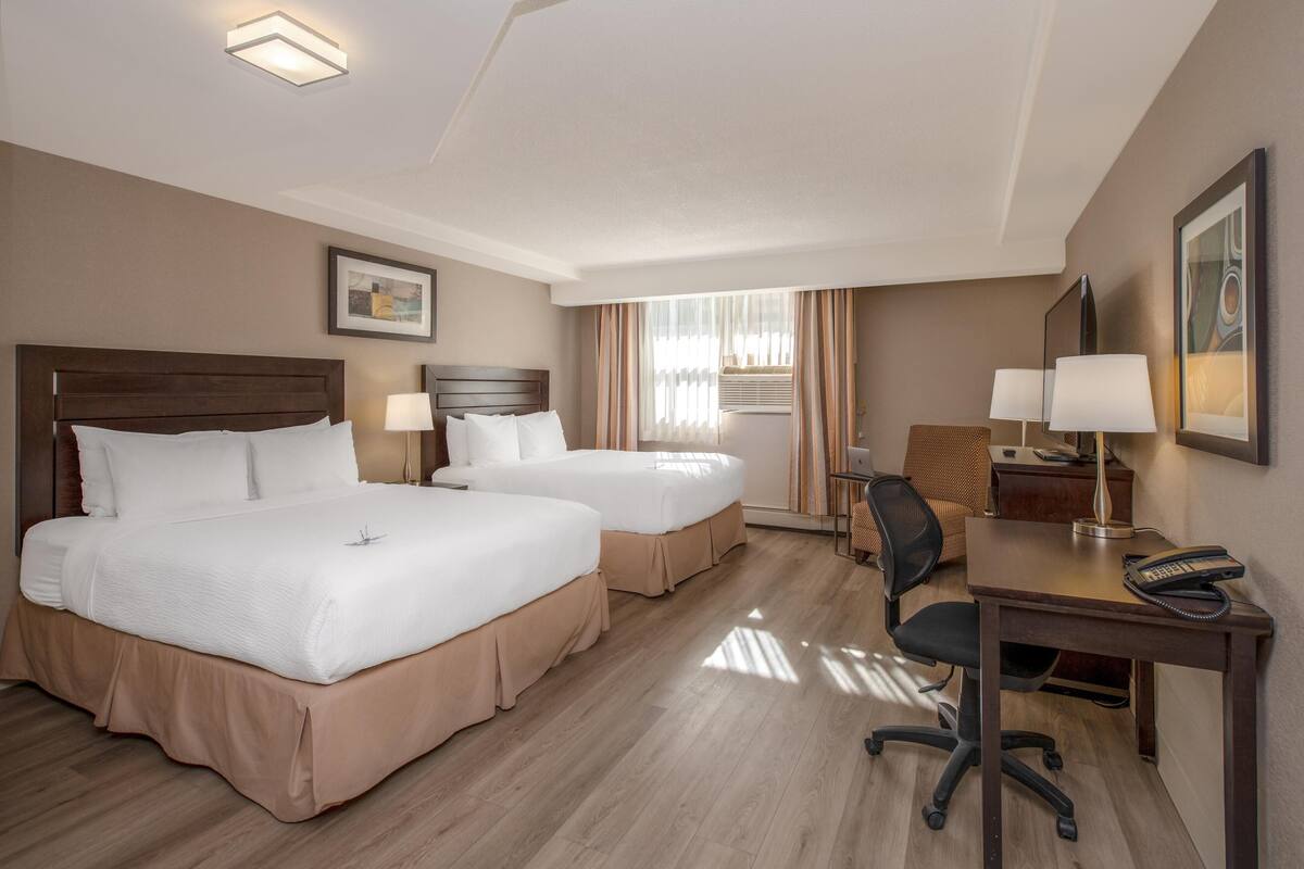 A hotel room with two beds, a desk, a chair, a lamp, and a framed picture on the wall.