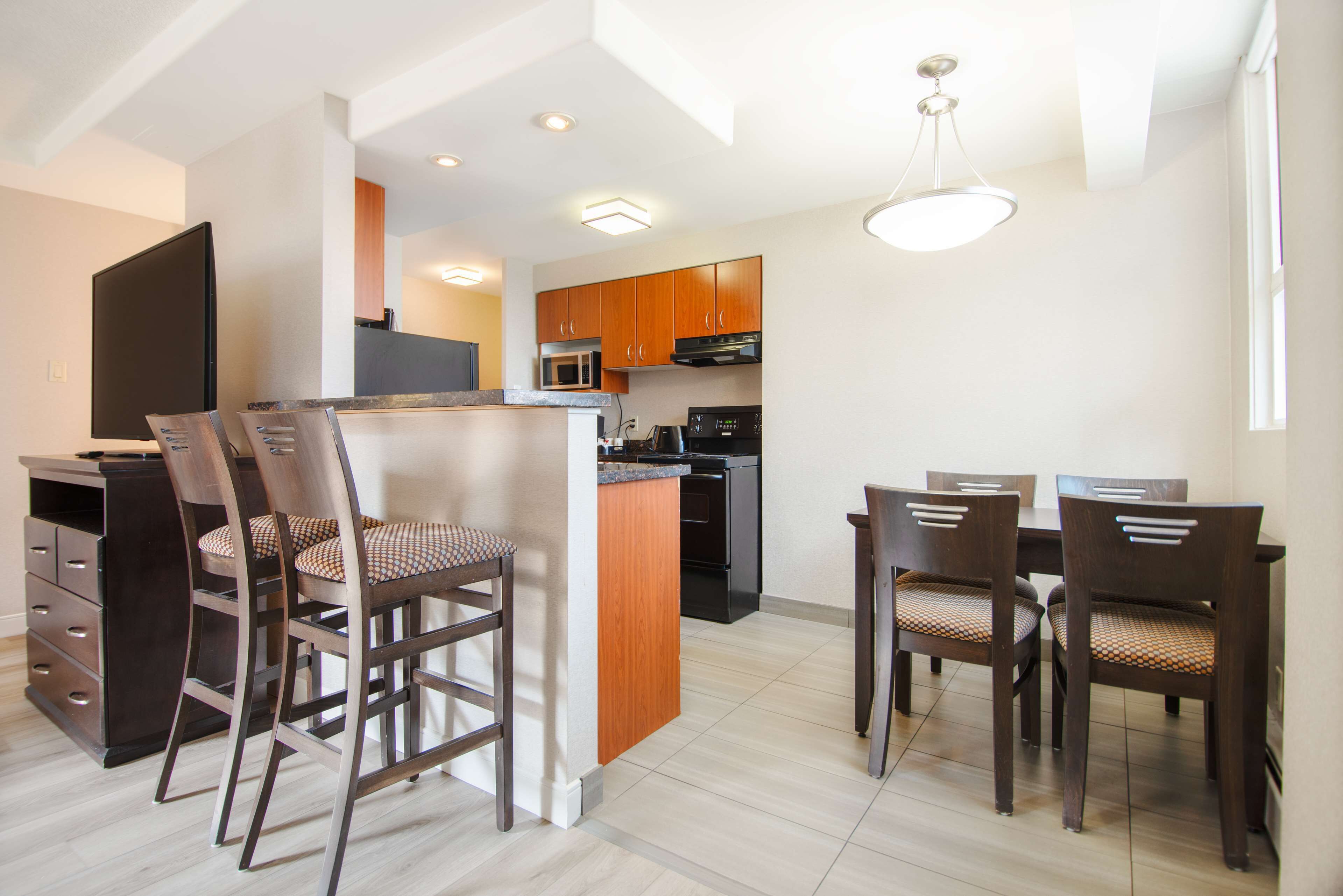 A modern kitchen with wooden cabinets, a microwave, and a stove. There is a dining area with a table and chairs.