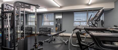 A modern gym with various exercise equipment, large windows, and a clean, organized layout.