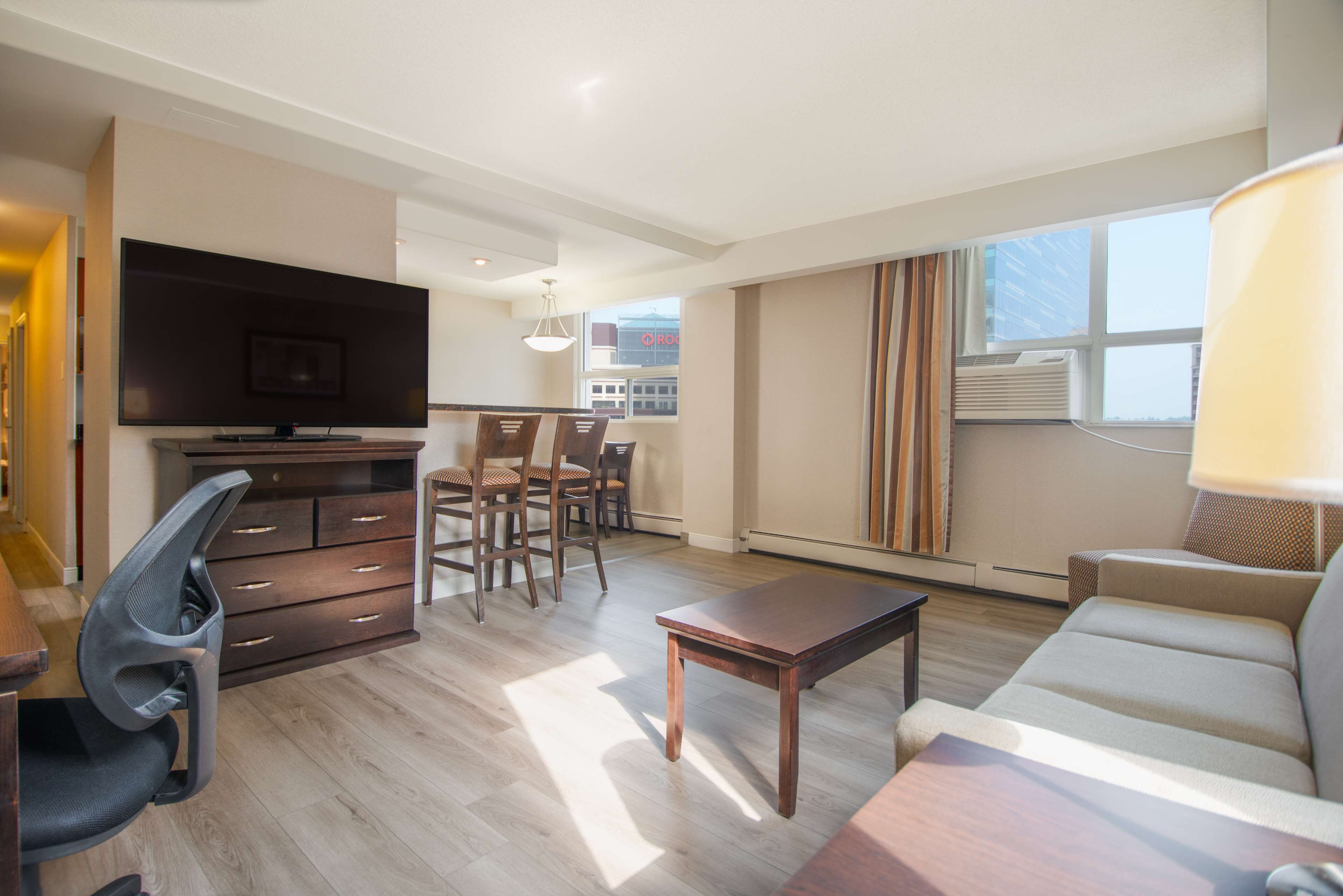 Een moderne woonkamer met een flatscreen televisie, houten meubels, een bank en een eethoek met stoelen.