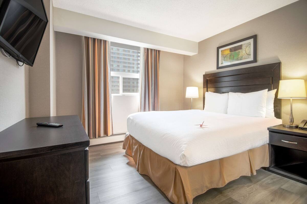 A hotel room with a large bed, a desk, a TV mounted on the wall, and a window with curtains.
