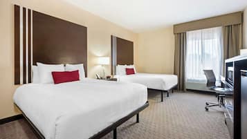 A hotel room with two beds, a desk with a chair, a TV, and a large window with curtains.