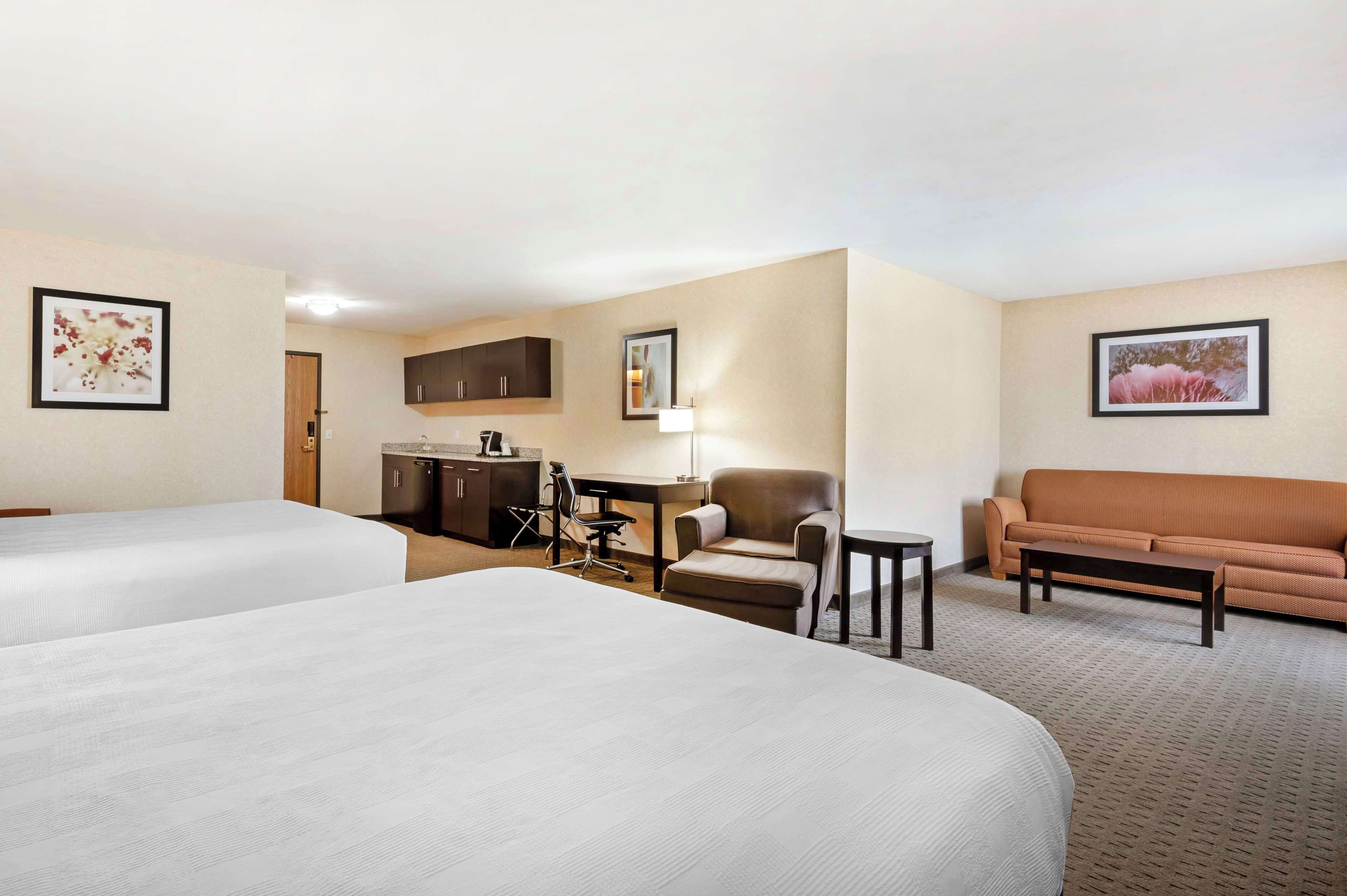 A hotel room with two beds, a desk, a chair, a sofa, and a lamp.
