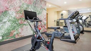 Een overdekte sportschool met hometrainers, loopband en een televisie aan de muur.