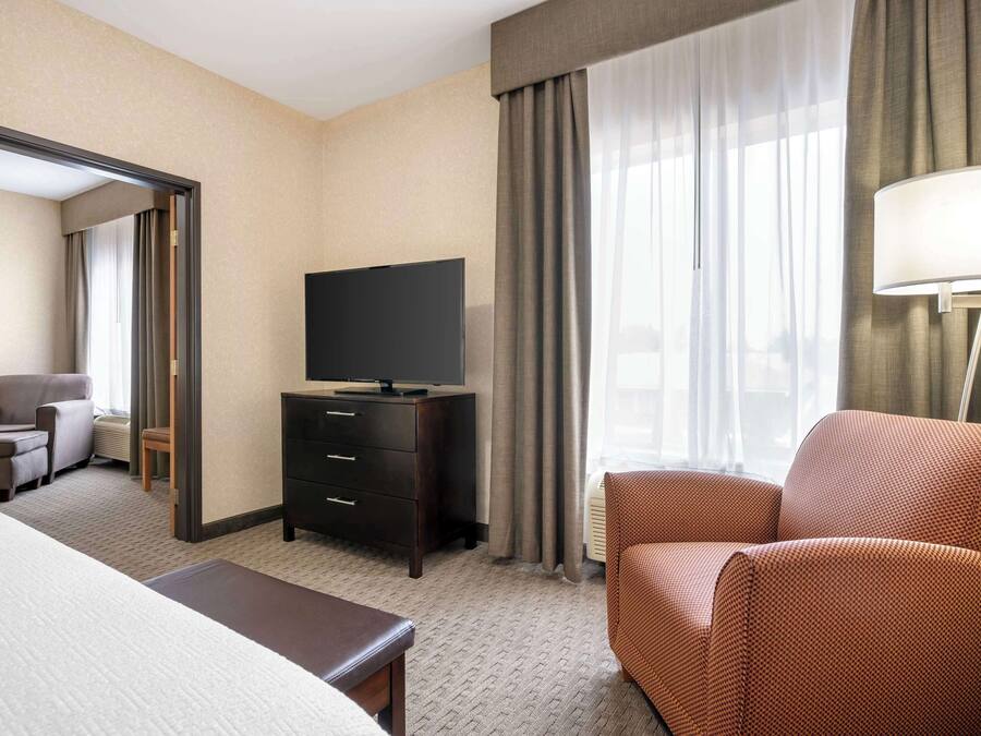 Ein Hotelzimmer mit Bett, Fernseher auf einer Kommode, Stuhl und Lampe.