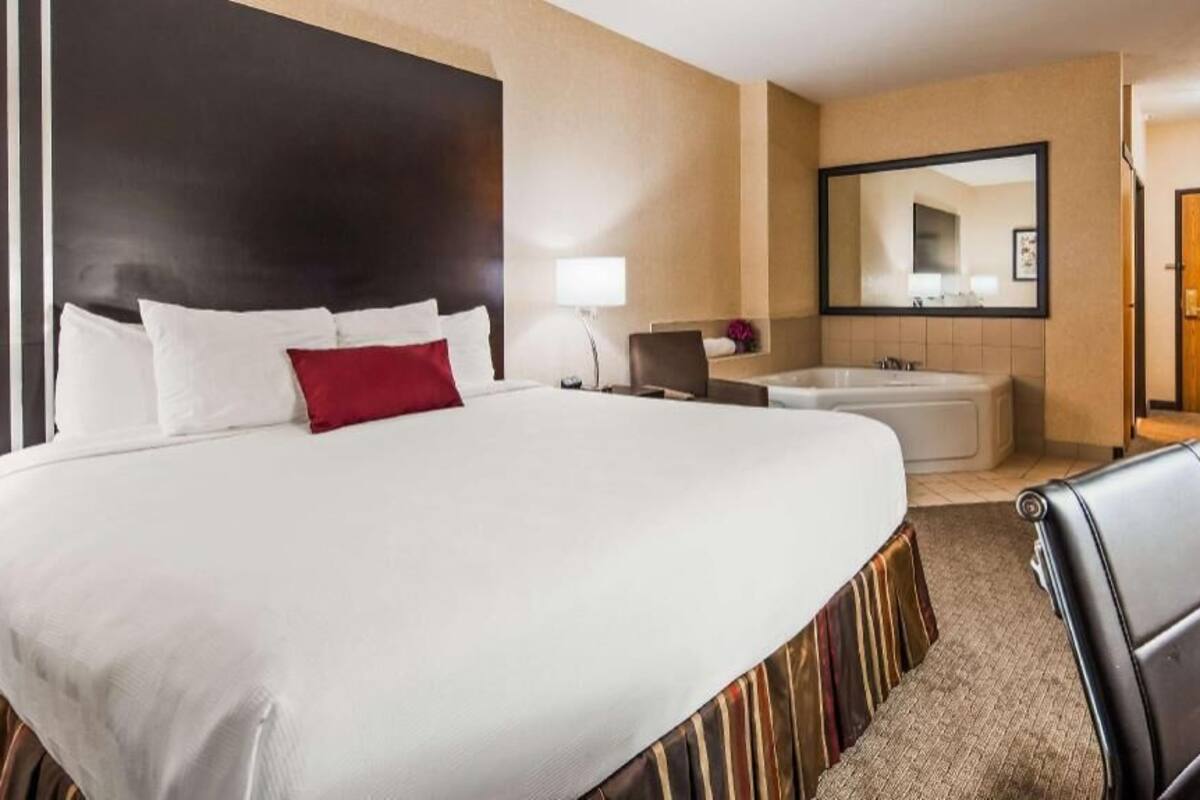 A hotel room with a large bed, a sitting area with a chair, a desk, a bathtub, and a TV.