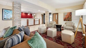 Un hall de hotel con mostrador de recepción, área de estar con sofás y otomanas, y obras de arte en las paredes.