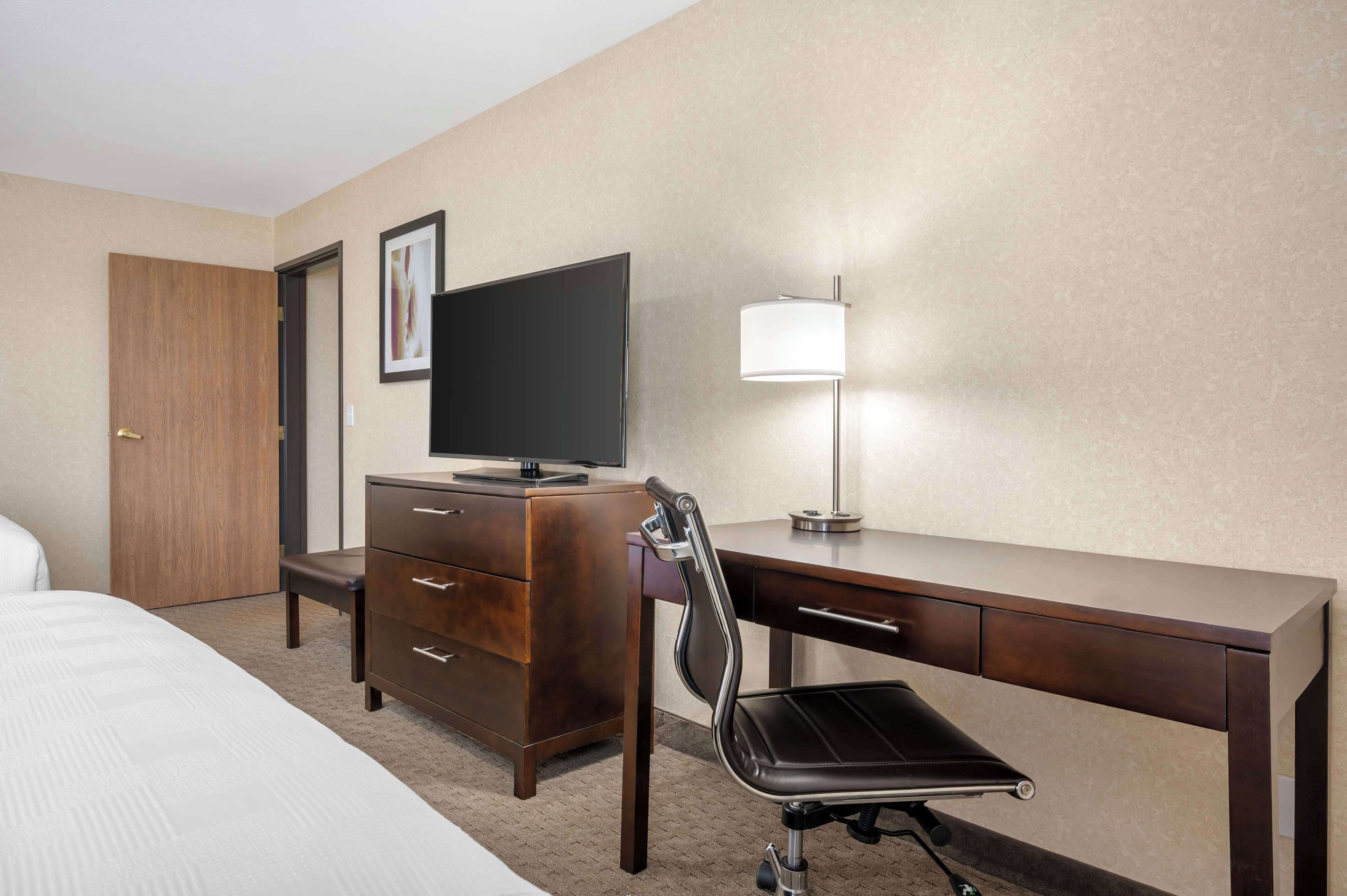 A hotel room with a bed, a desk, a chair, a television, and a lamp.
