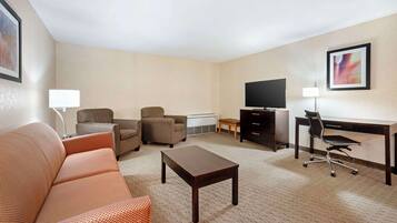 Quarto de hotel com sofá, duas poltronas, escrivaninha com computador, televisão e luminária.