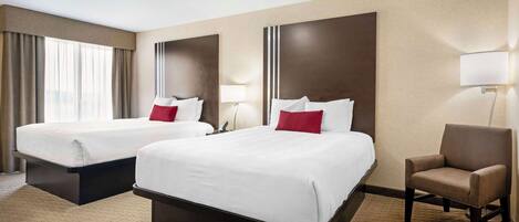 A hotel room with two beds, a chair, and a lamp.