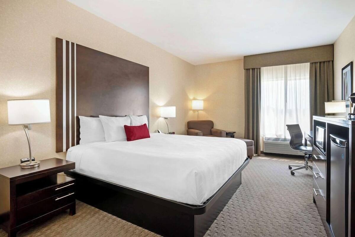 A hotel room with a large bed, bedside lamps, a desk with a chair, and a view of the outdoors through the window.