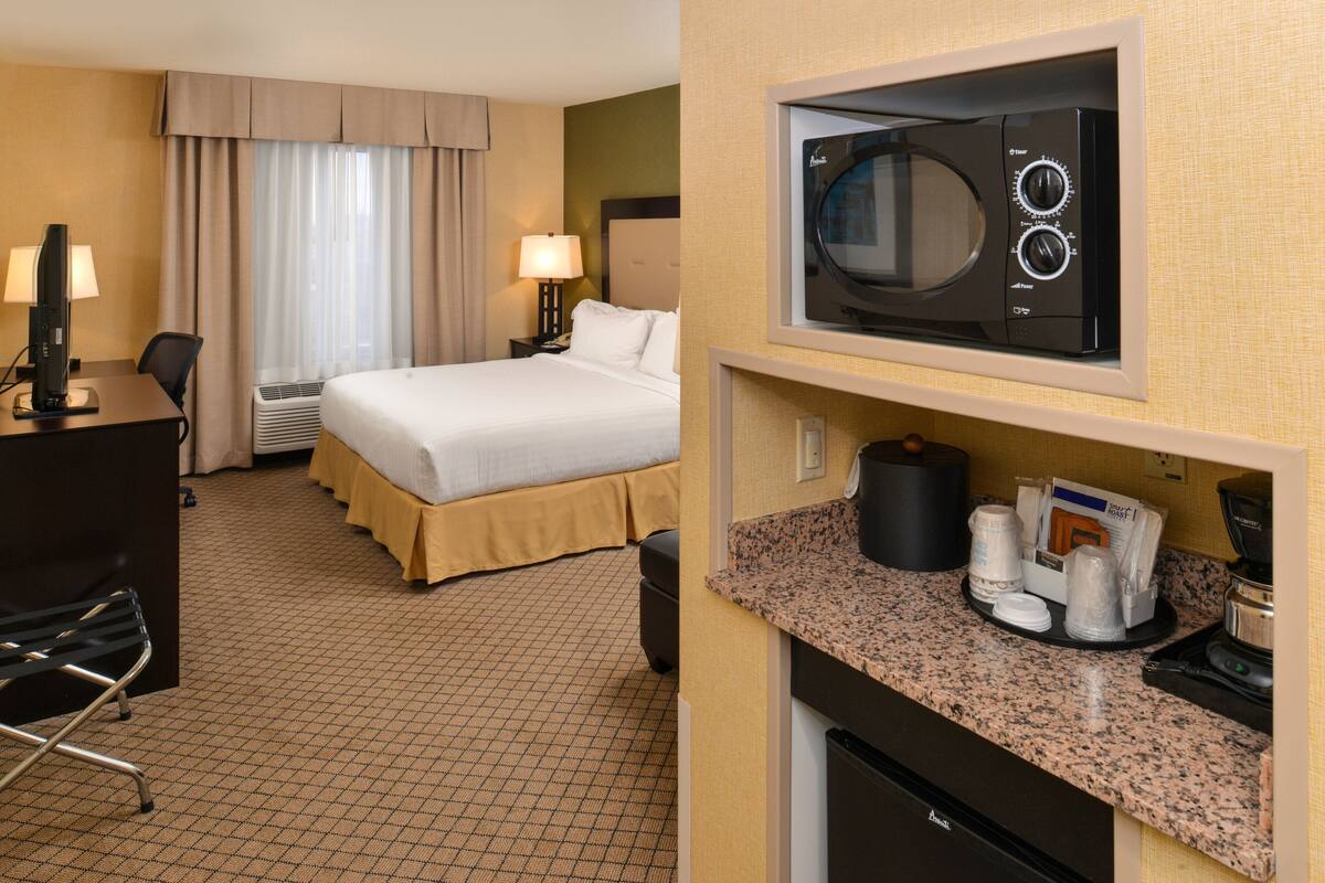 A hotel room with a bed, desk, chair, microwave, and coffee maker.