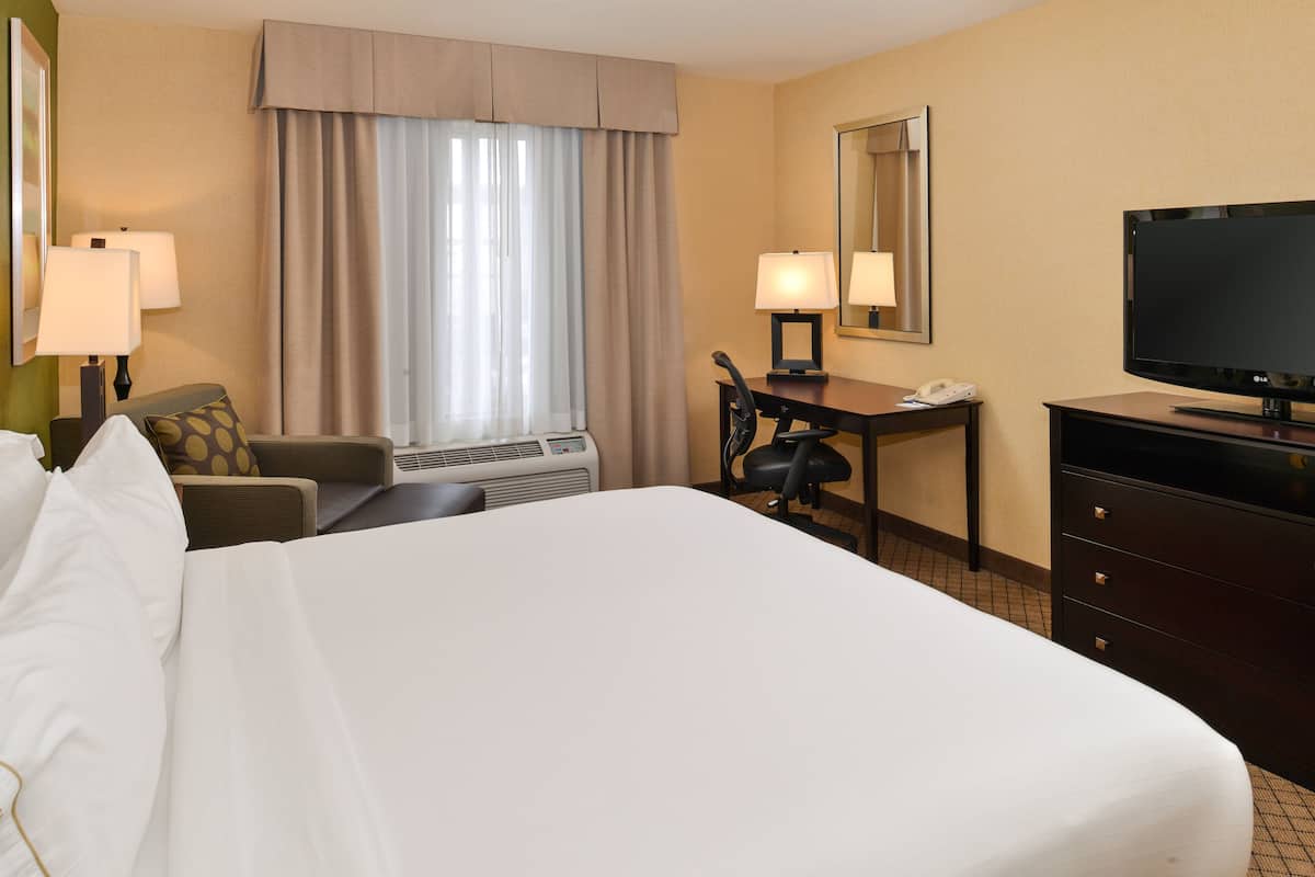 A hotel room with a large bed, a desk with a chair, a television, and a window with curtains.