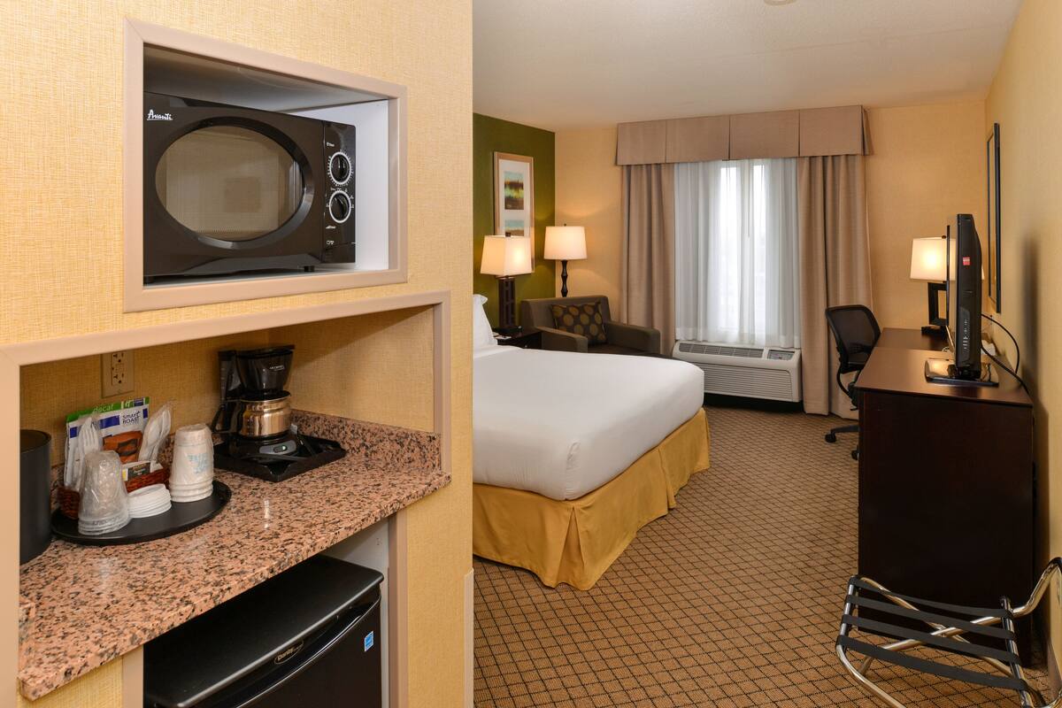 A hotel room with a bed, a desk, a microwave, a coffee maker, and a TV.
