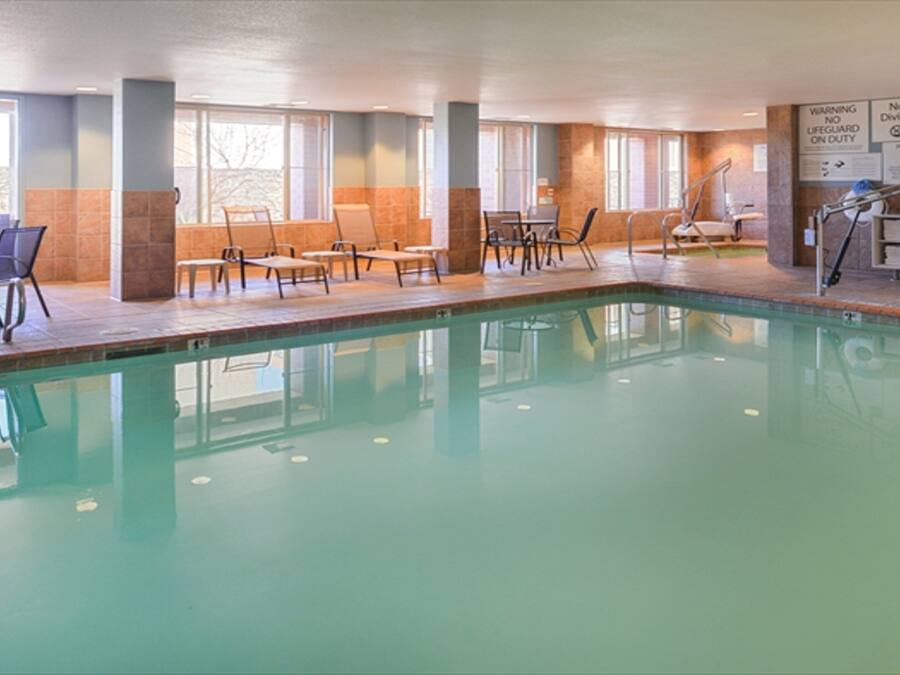 A swimming pool with lounge chairs and tables, surrounded by windows and safety signs.