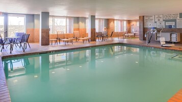 Una piscina con sillas y mesas de descanso, rodeada de ventanas y señales de seguridad.