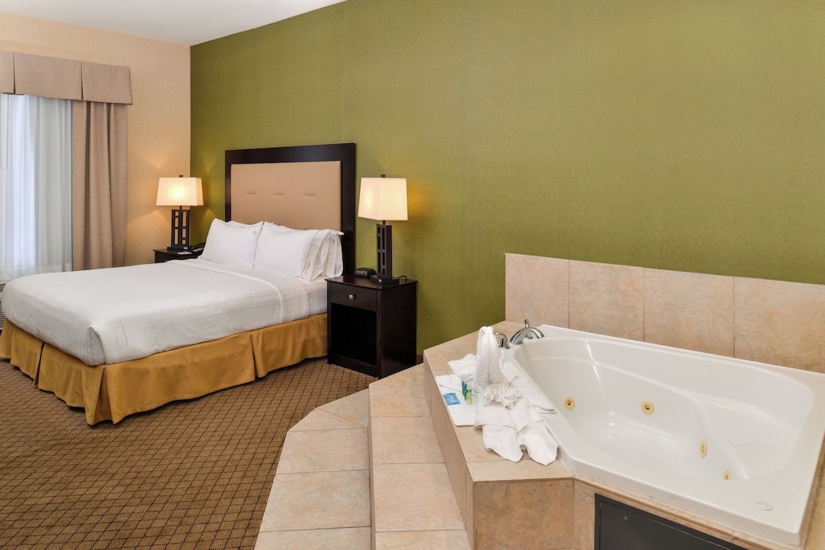 Habitación de hotel con cama, dos mesitas de noche con lámparas, una bañera grande y una pared verde.