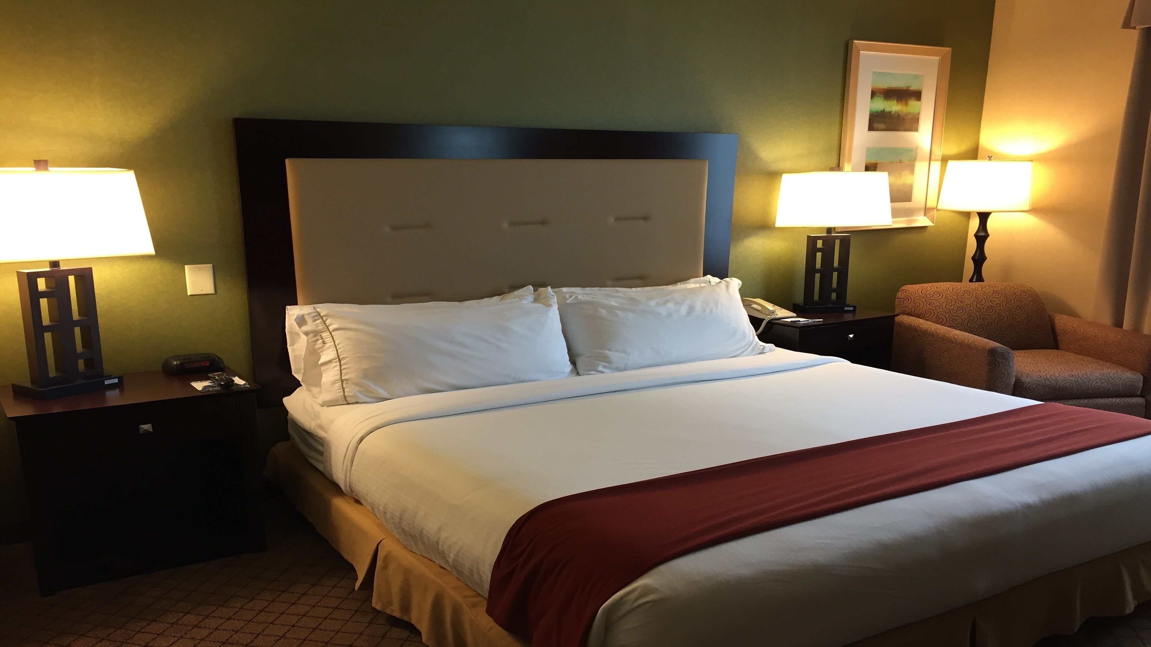 A hotel room with a large bed, two bedside tables, a chair, and two lamps.