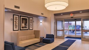 A lobby with a sofa, chairs, framed artwork, and a large door leading outside. - Holiday Inn Express Sacramento Airport Woodland by IHG (Woodland)